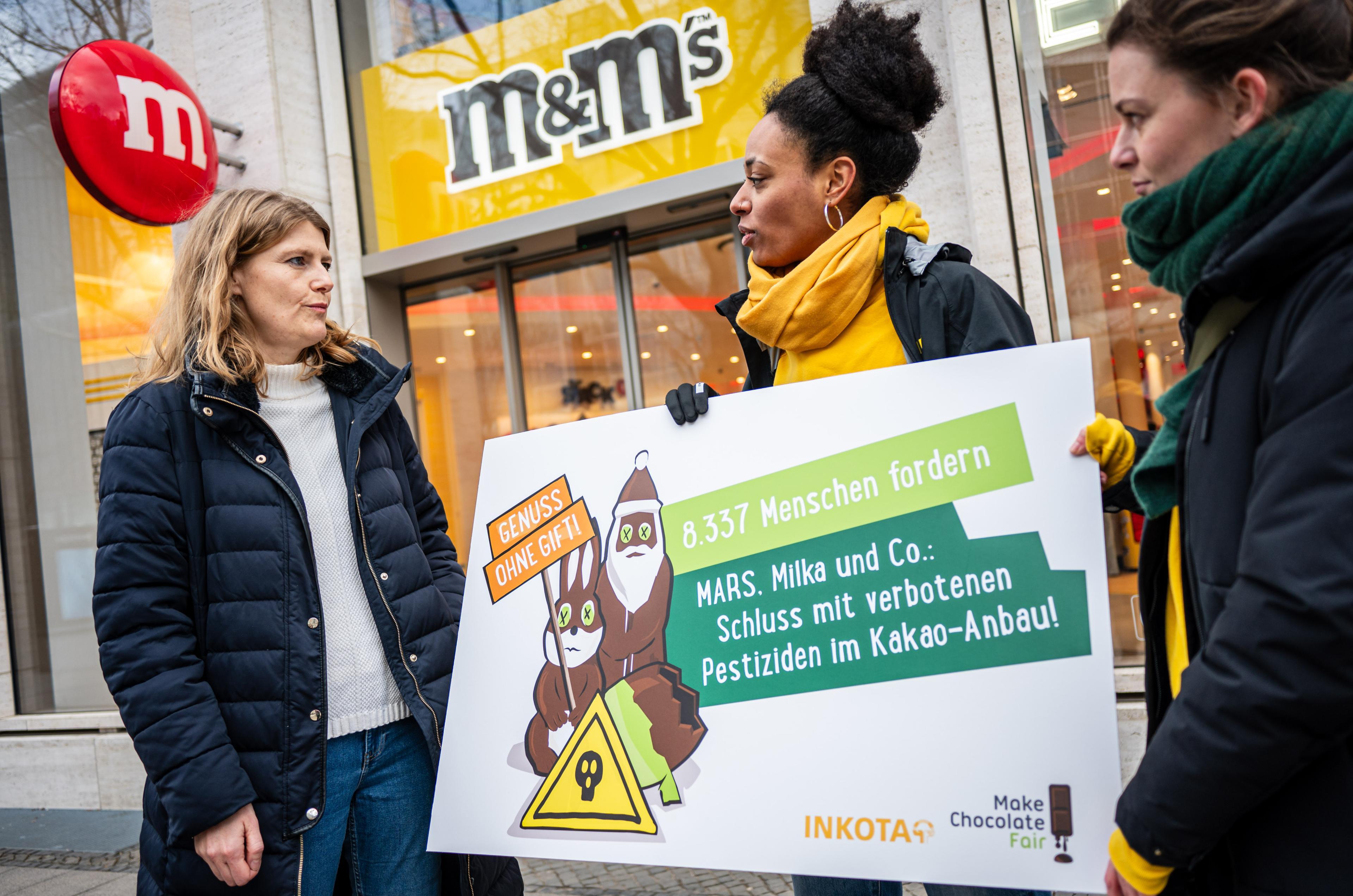 Keshia Acheampong und Juliane Bing übergeben bei der Kundgebung und Protestaktion vor dem Mars M&M Store in Berlin zum Abschluss der "Genuss ohne Gift"-Aktion die Unterschriften an MARS Vertreterin